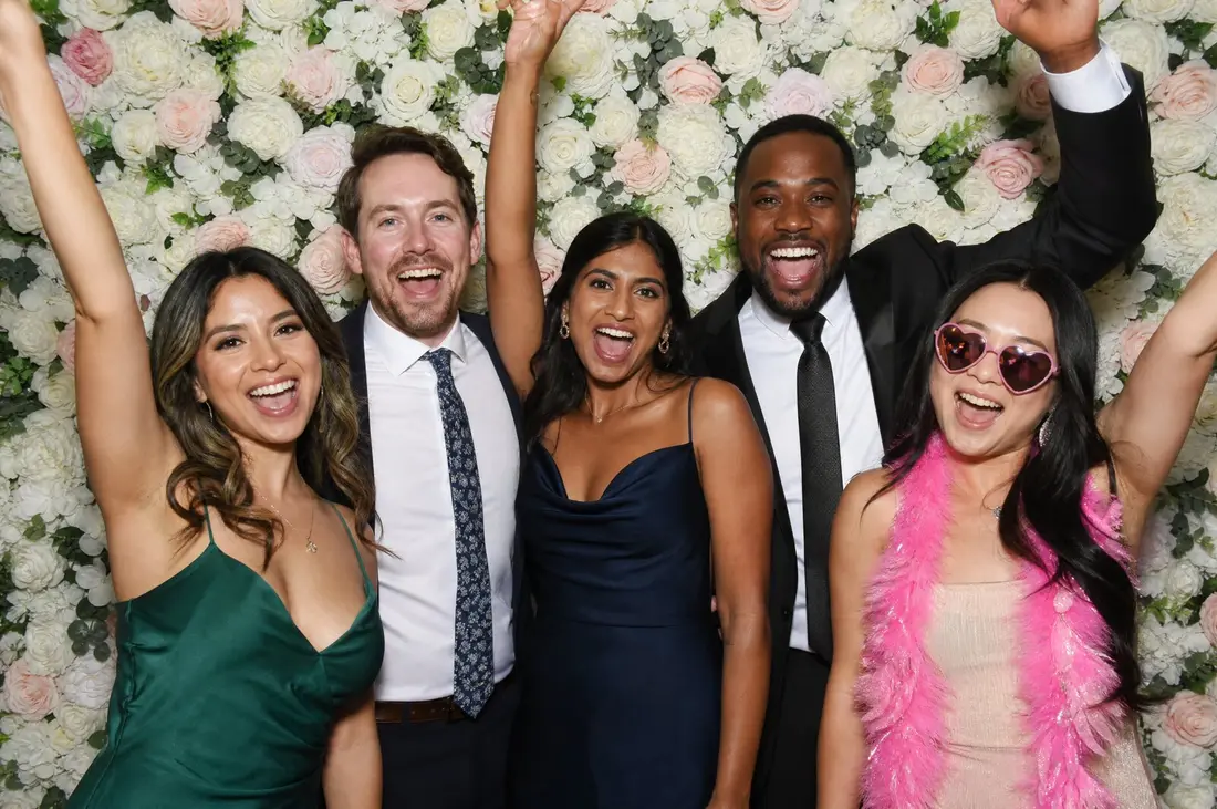 Wedding guests with props in front of a flower wall at an open-air photo booth